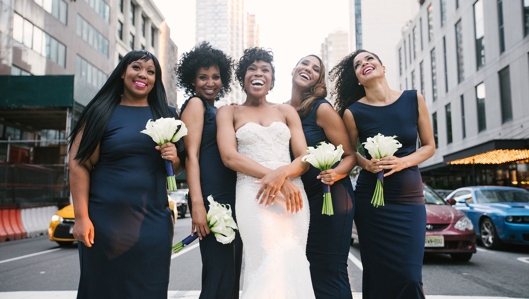 Ahkilah in her wedding dress with bridesmaids holding flowers on a street crosswalk
