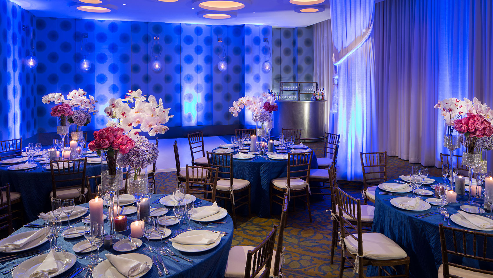 Venue space set up for event with round tables, tall floral arrangements, and dance floor
