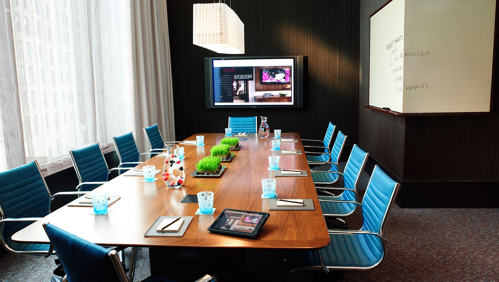 Venture Boardroom with large wooden table with notepads facing presenter screen and wrap-around whiteboard