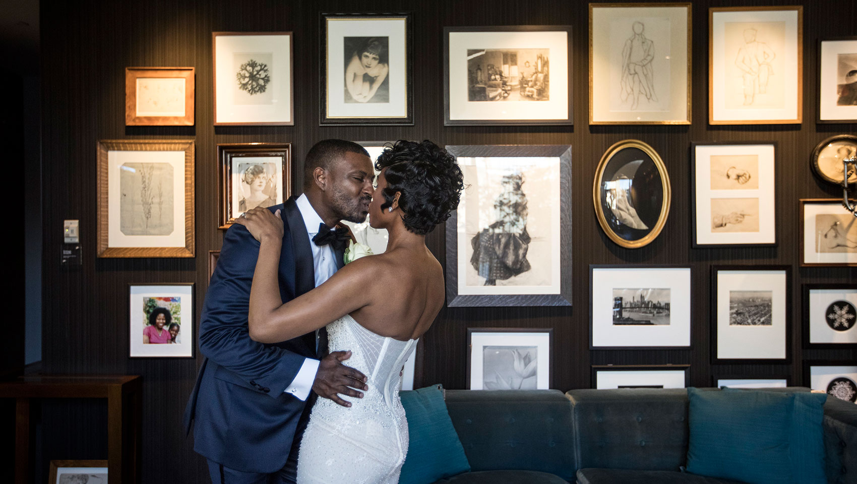 Bride and groom kissing in front of wooden wall with framed pictures and portraits