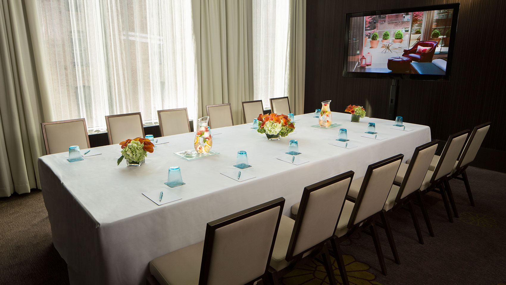 Meeting room table with notepads, glasses, and floral arrangements in the center of the table