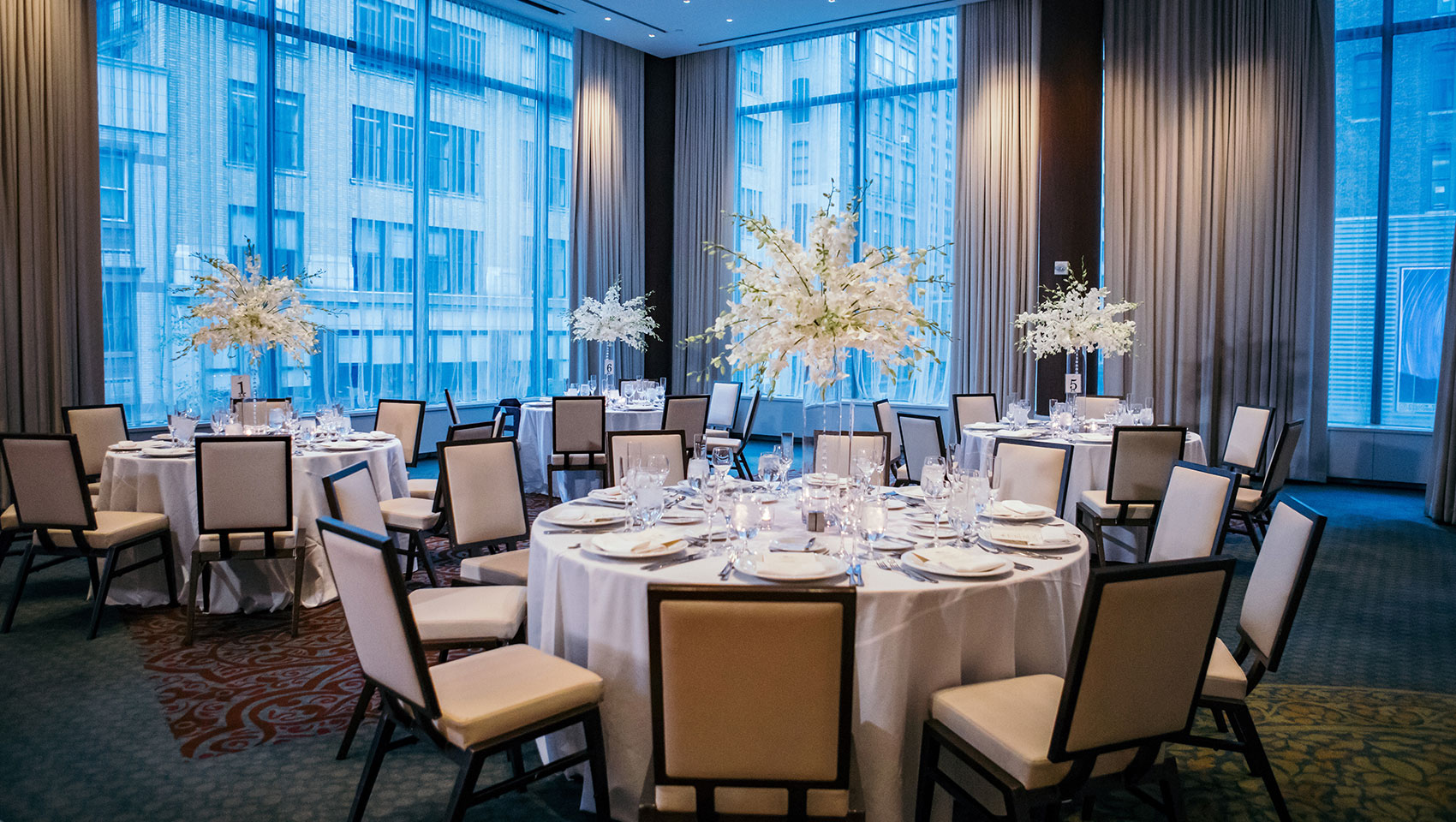 Ventana wedding set up with round tables that have place settings and tall floral arrangements next to large windows with city views