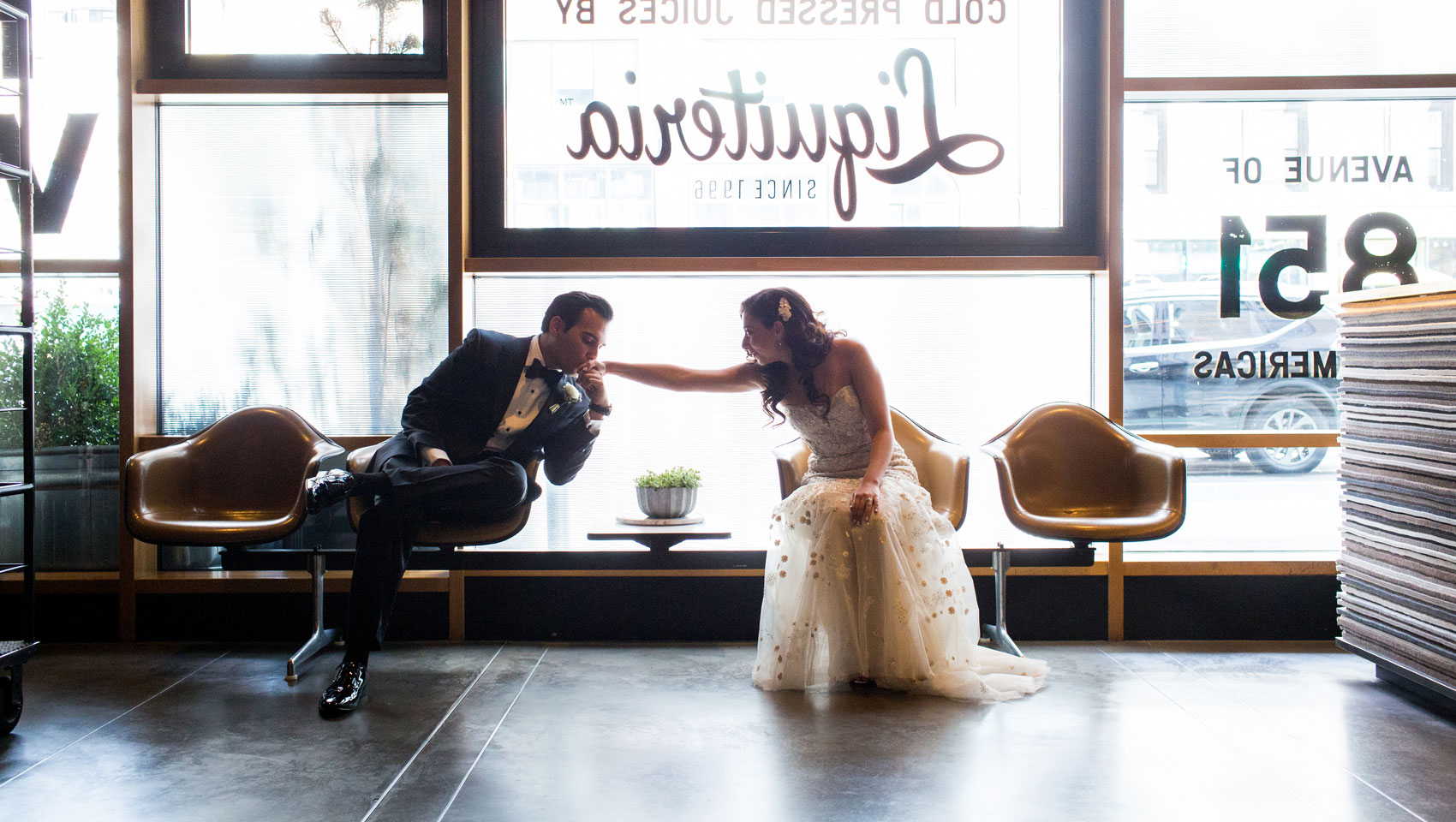 Groom kissing bride's hand while sitting in chairs at Kimpton Hotel Eventi lobby
