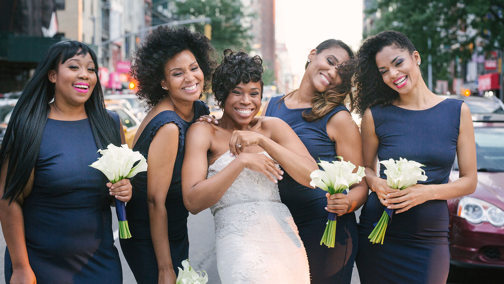Ahkilah in her wedding dress with bridesmaids holding flowers on a street crosswalk