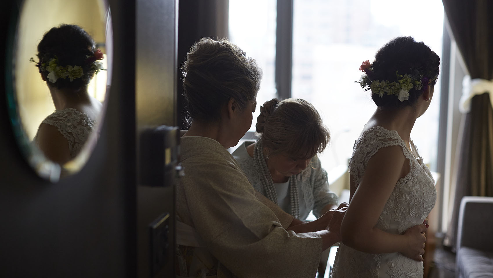 Two women helping Yoko adjust her dress from behind