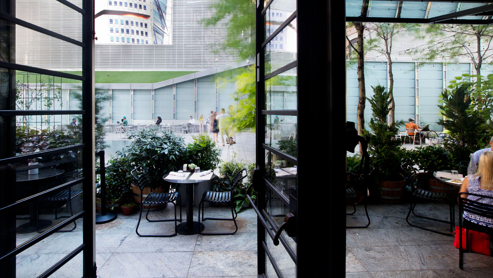 Big screen plaza at Kimpton Hotel Eventi seen through large open windows with plaza greenery and seating