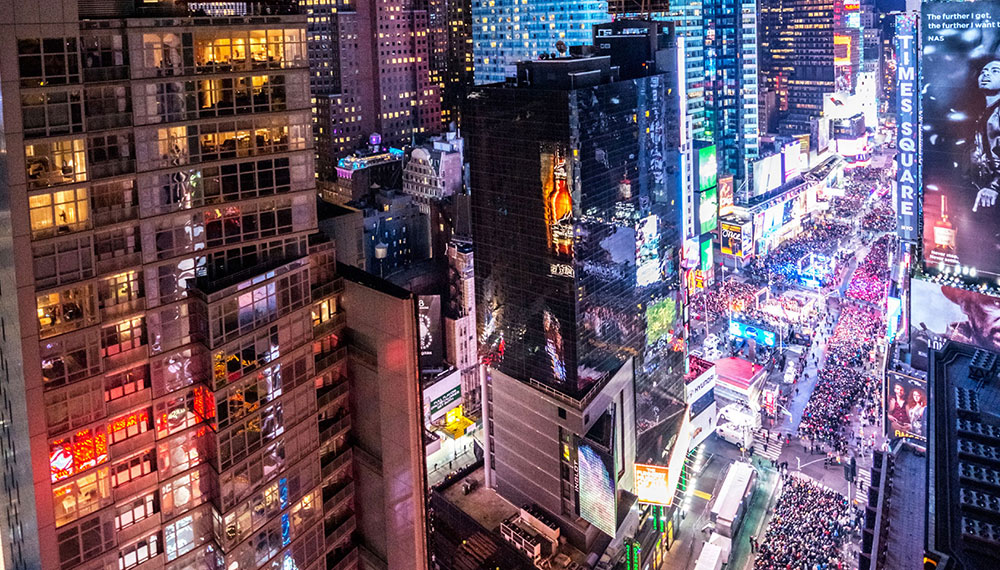 Times Square during nighttime with large crowds in the streets between tall buildings