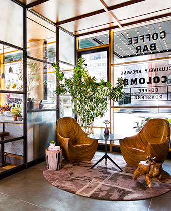 Lobby seating with wooden chairs against sunlit glass walls