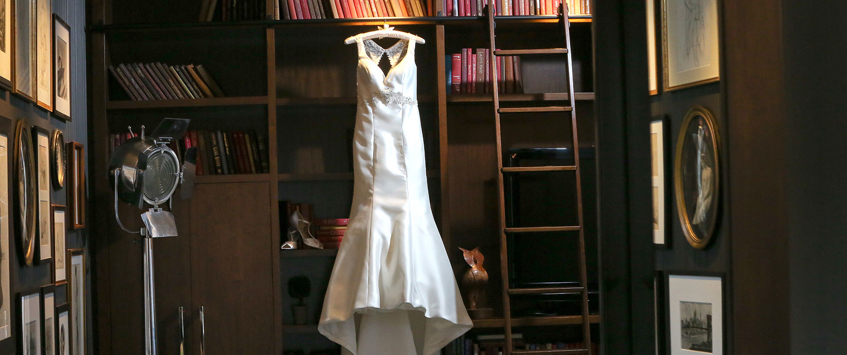 Bridal dress next to a ladder, hung from a wooden bookcase