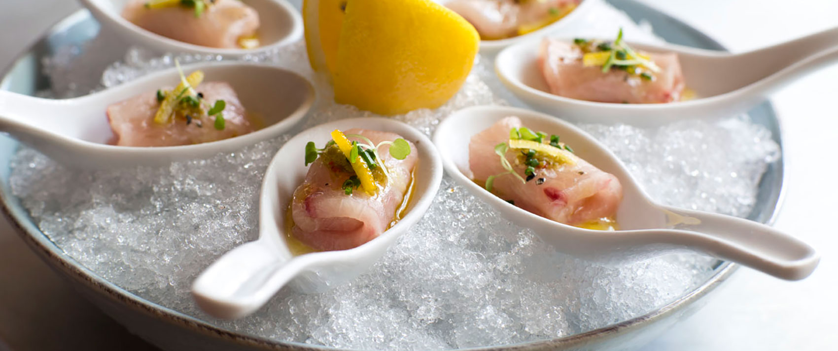 Seafood on spoons in a chilled bowl with a lemon wedge in the middle